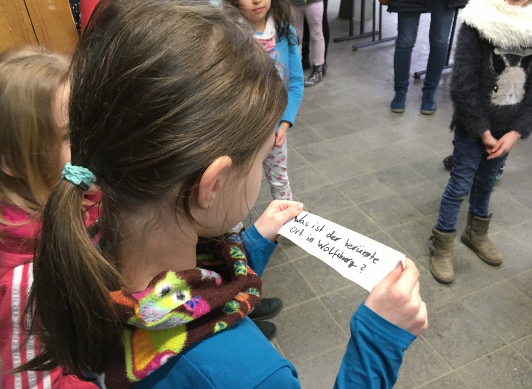 Kind hält Zettel mit Text in der Hand.