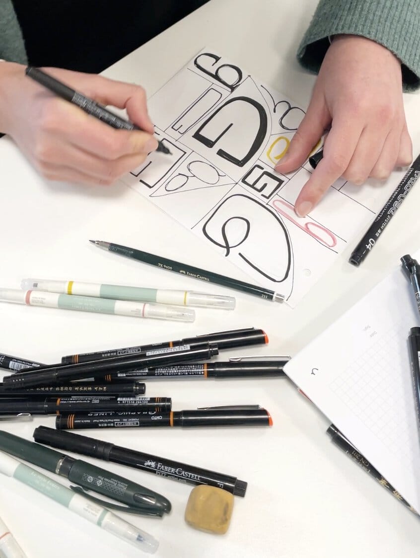 Auf einem Tisch liegen mehrere Blätter mit ein paar Schriftexperimenten drauf.