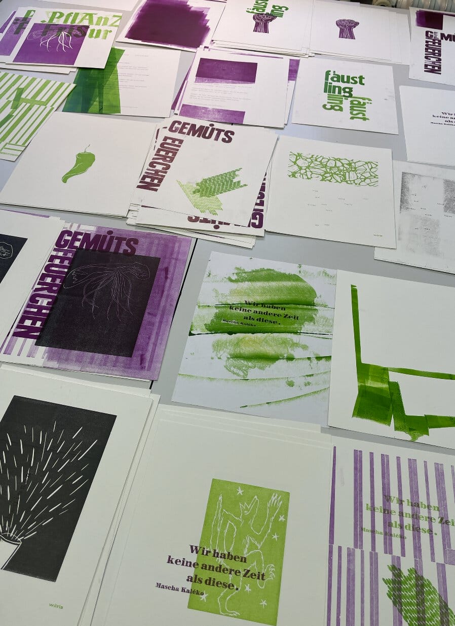 Auf einem Tisch ausgebreitet liegen viele verschiedene Drucke in Lila und Grün.