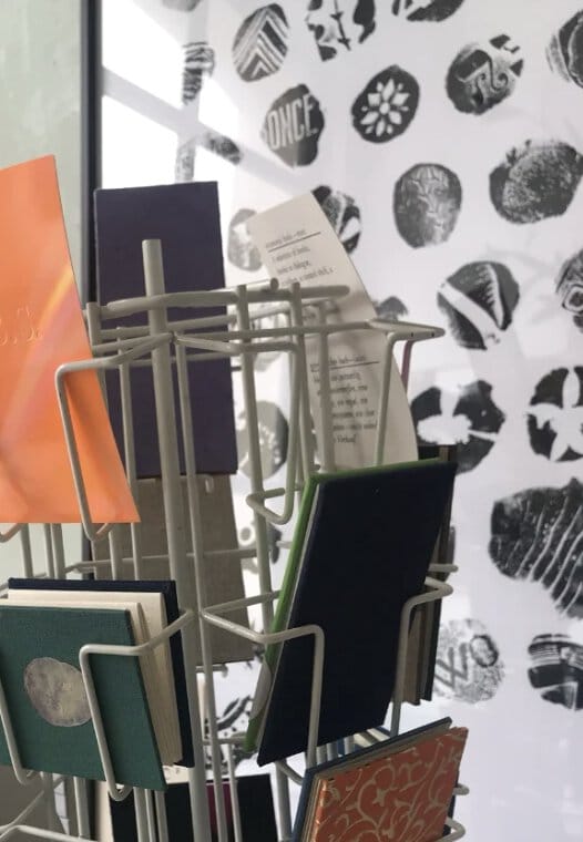 Im Vordergrund: Ein Ständer mit Büchern und im Hintergrund ein Plakat mit gestempelten Motiven